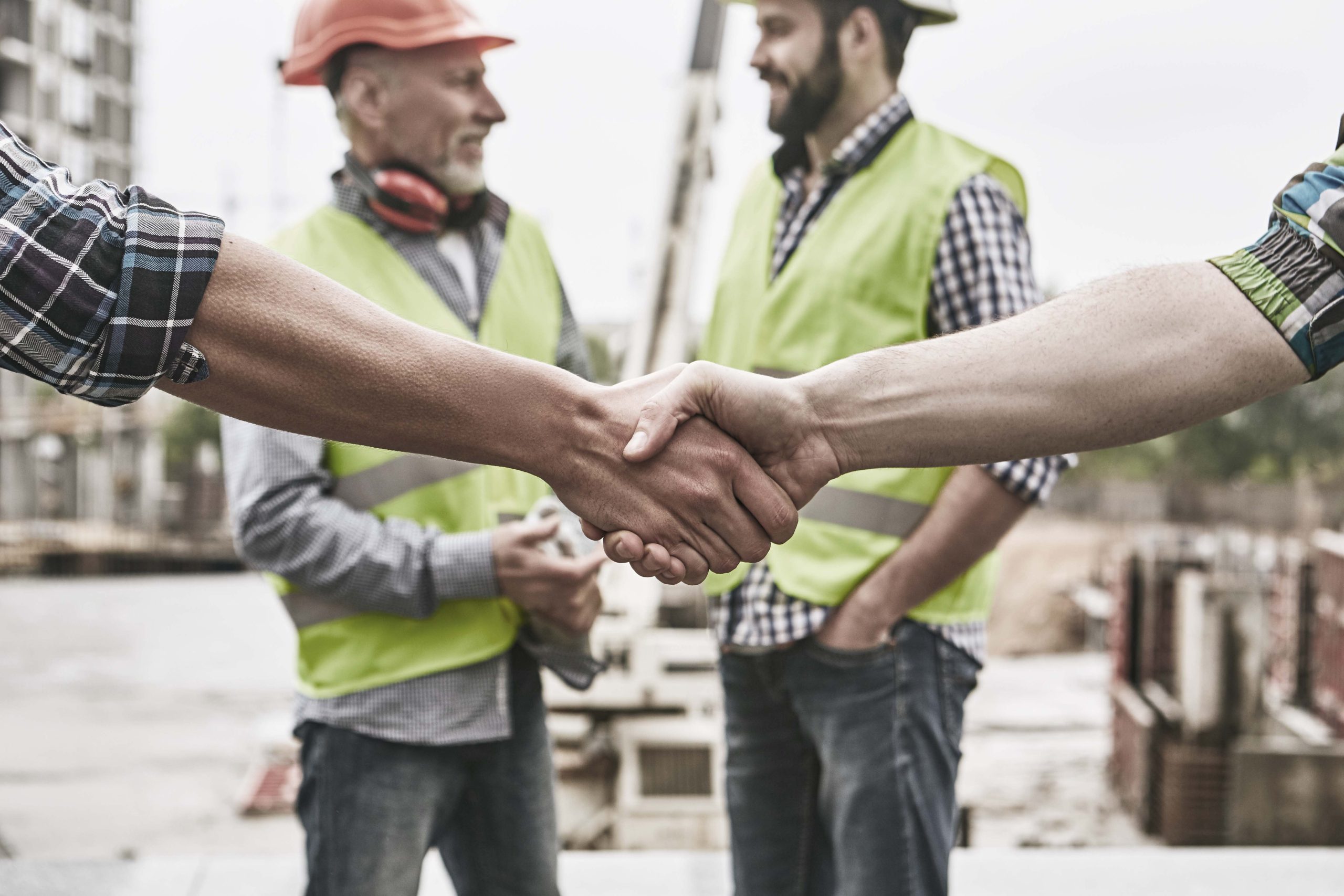 we-did-it-close-up-photo-of-builders-shaking-hands-against-cheerful-colleagues-while-working-together-at-construction-site-team-work